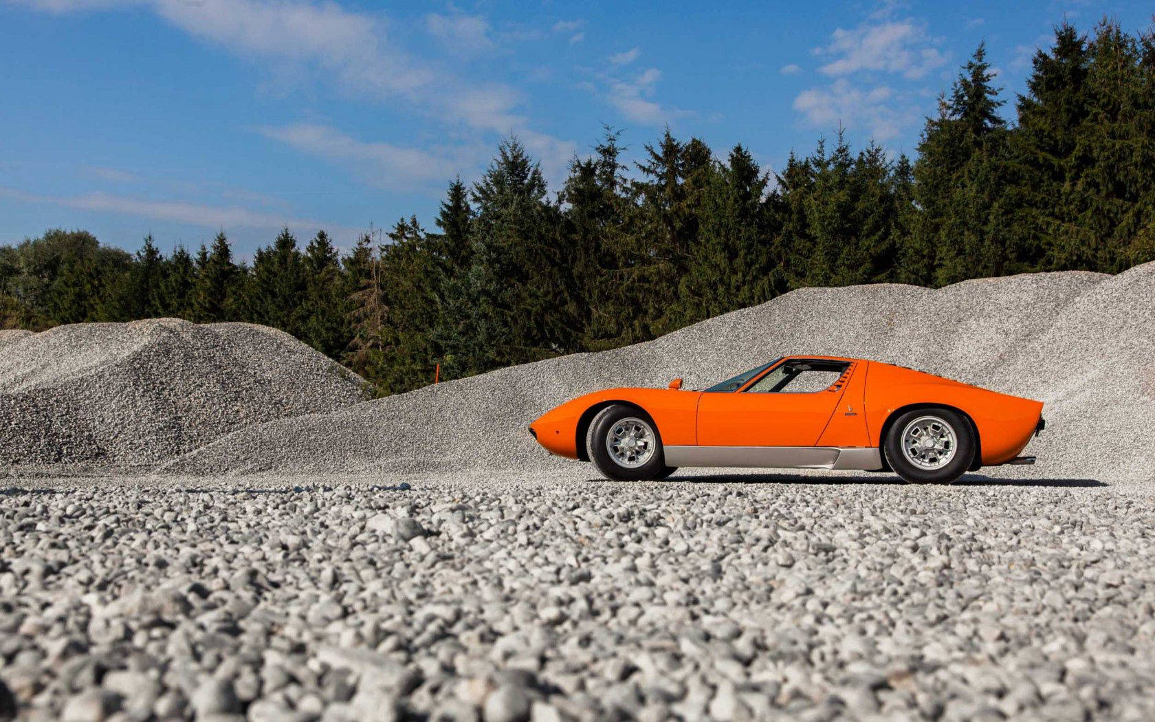 Erinomainen oranssi Lamborghini Miura soratiellä. Taustakuvat