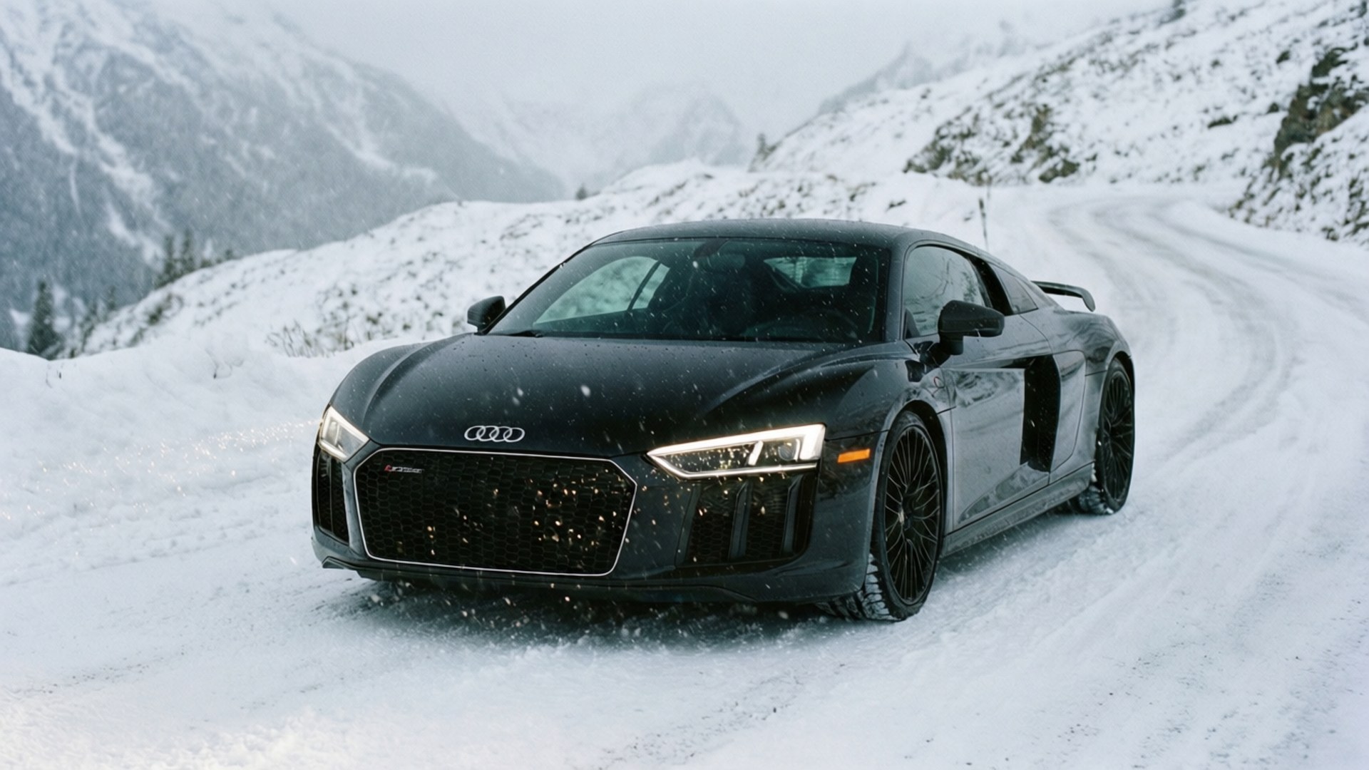 Musta Audi R8 ajaa lumisella alppitiellä, ja lunta sataa. — Hienot autot GIF Taustakuvat