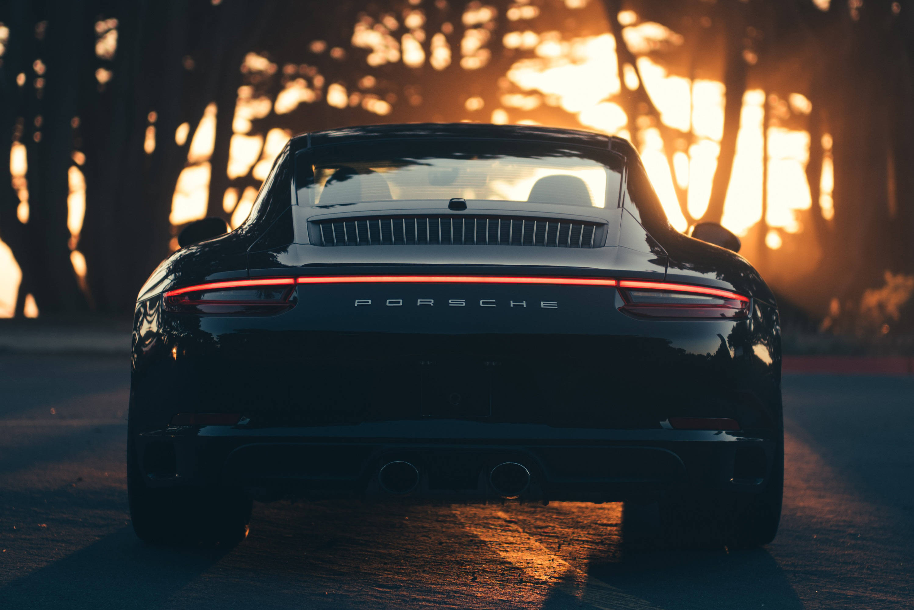 Musta Porsche 911 ihailemassa auringonlaskua Taustakuvat