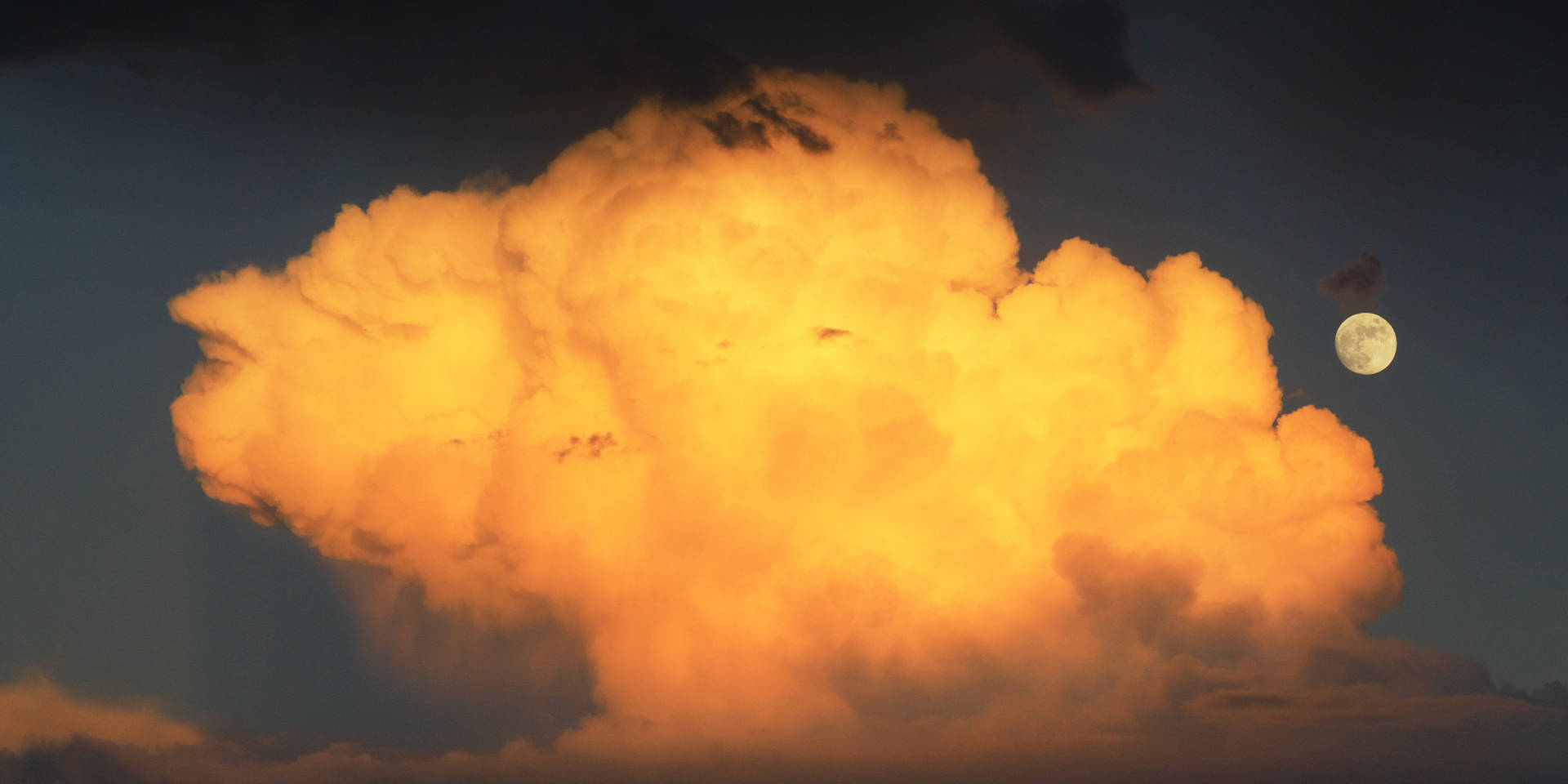 Kuu ja pilvet heijastavat auringonvaloa auringonlaskusta. Täysikuu näkyy ennen auringon laskua.