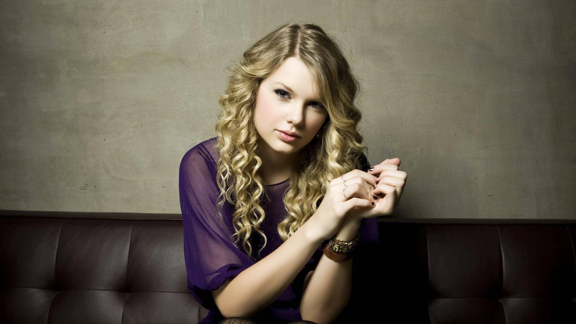 Istuva kiharainen Taylor Swift violetissa mesh-topissa -taustakuva.