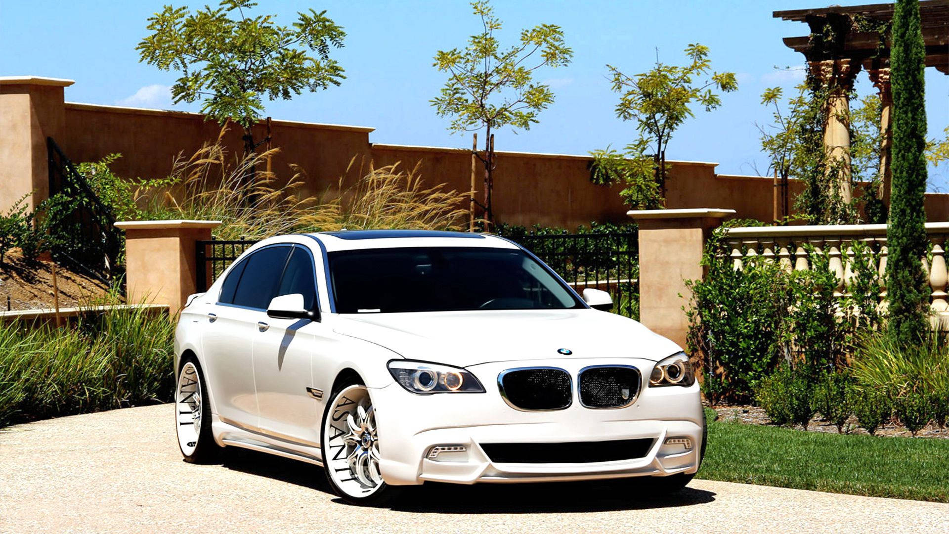 Valkoinen BMW 7 F01 -auto Asanti-vanteilla portilla -taustakuva