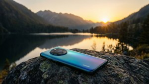 Huawei-puhelin kalliolla vuoristojärven yllä auringonlaskun aikaan, tyyni maisema.