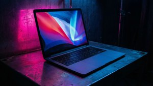 Kyberpunk-henkinen MacBook neonheijastuksineen pimeässä huoneessa.